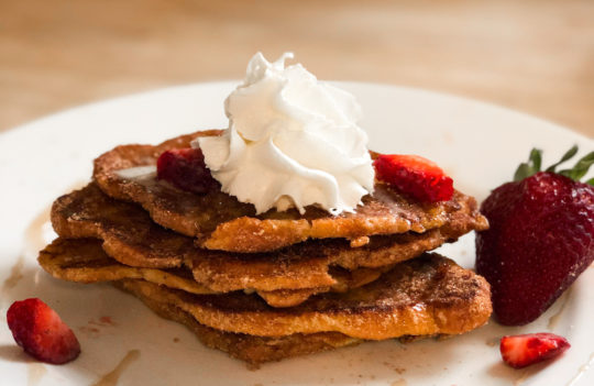 stacked churro croissant french toast with whipped cream and strawberries